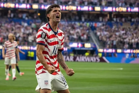 Christian Pulisic in a red and white striped jersey celebrates with clenched fists and an open mouth
